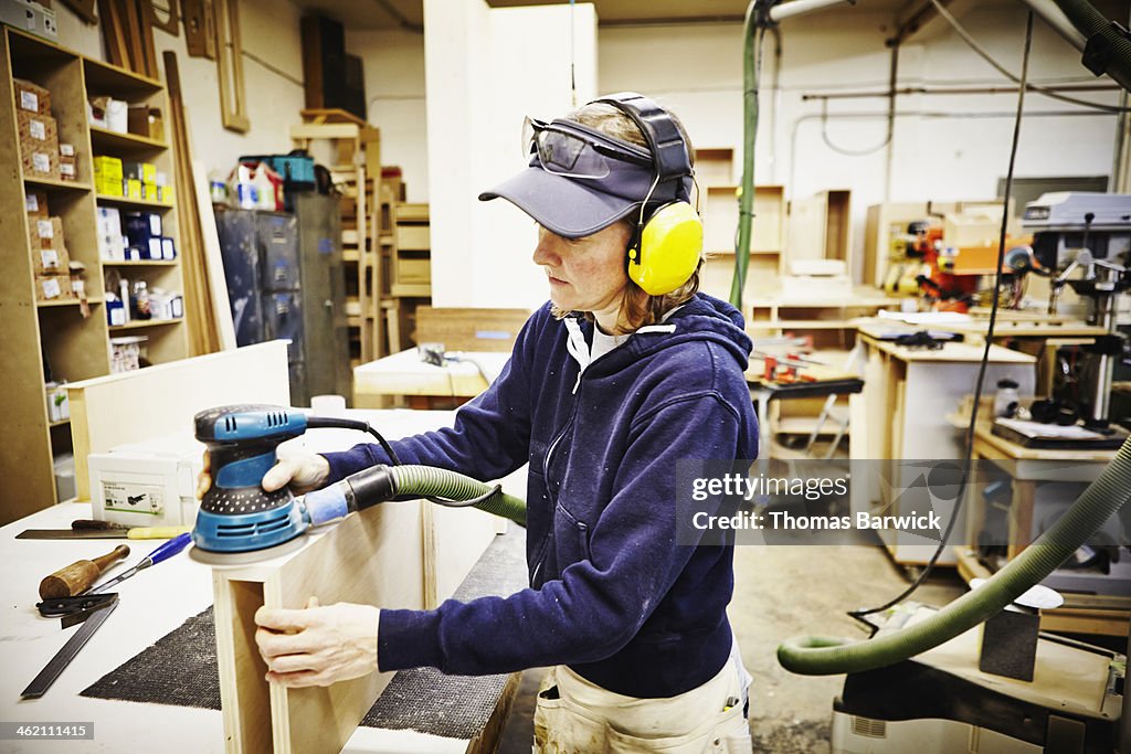 Female woodworker sanding edge of custom cabinet