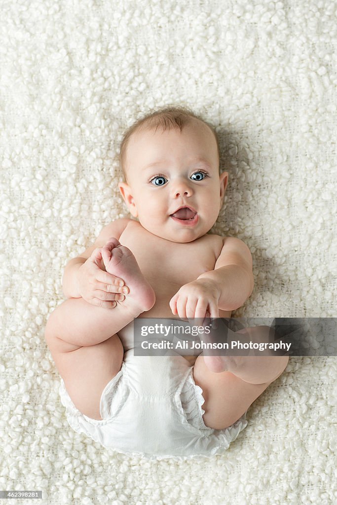 Baby lies on back and plays with feet