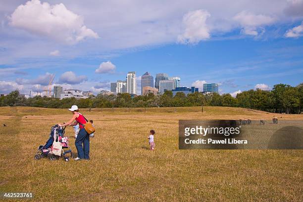 Mother with three children walking through city farm in London Docklands with Canary Wharf Financial Centre in the background.
