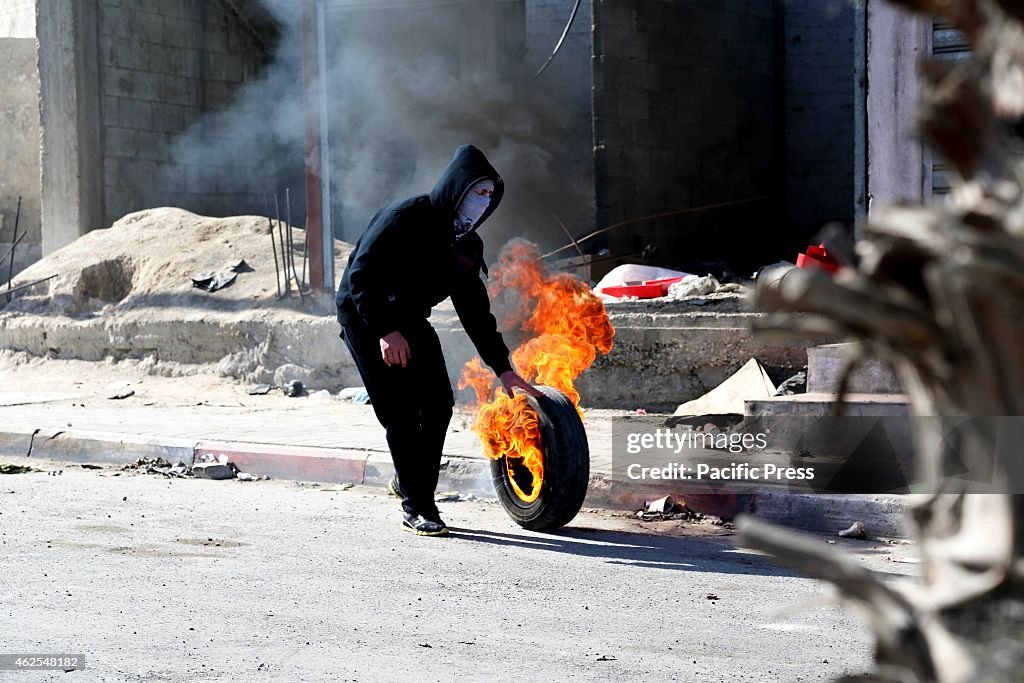 A masked Palestinian youth rolls a lit tire down the street...