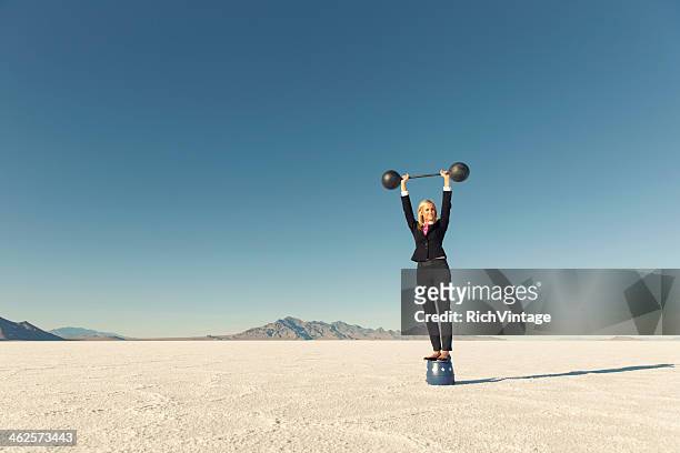woman dressed in business suit lifts barbell on salt flats - impact investing stock pictures, royalty-free photos & images