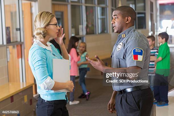 security or police officer talking with elementary school teacher - bewaker stockfoto's en -beelden