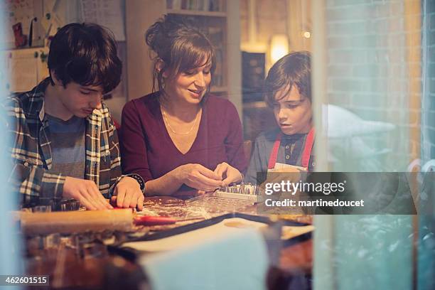 mother and sons making gingerbread cookie at home through window. - winter cooking stock pictures, royalty-free photos & images