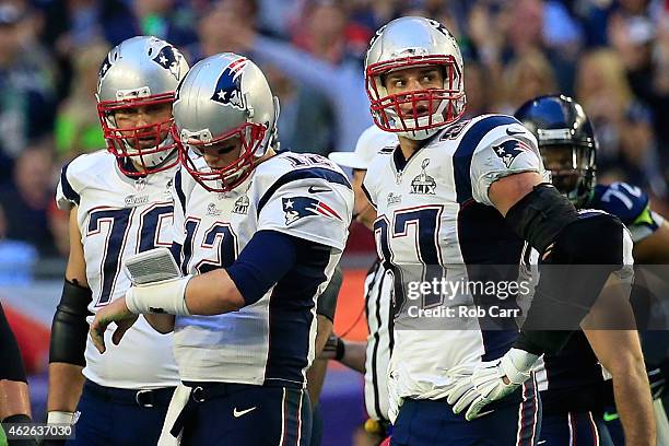 Tom Brady of the New England Patriots checks his play card as Sebastian Vollmer and Rob Gronkowski look on in the first quarter against the New...