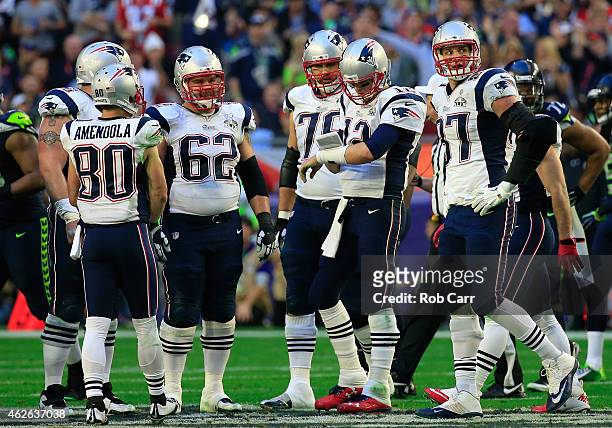 Tom Brady of the New England Patriots checks his play card as Sebastian Vollmer and Rob Gronkowski look on in the first quarter against the New...