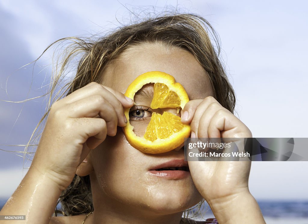 Young girl looking through slice of orange