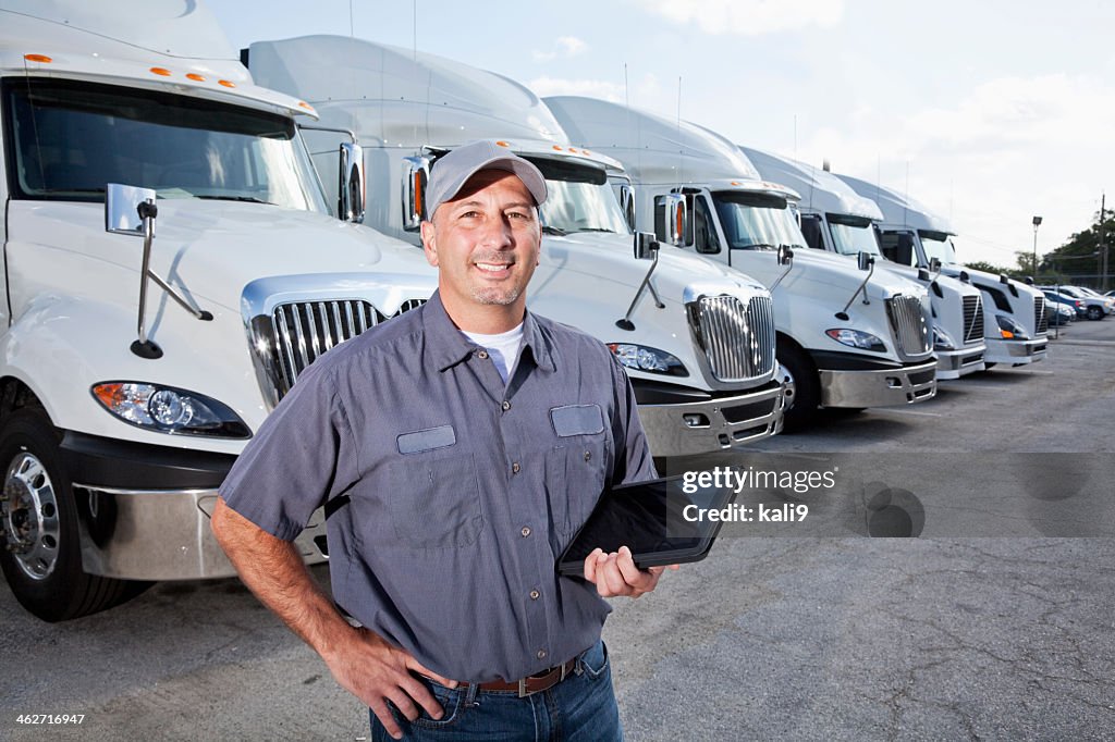 Big rig trucks behind man holding tablet