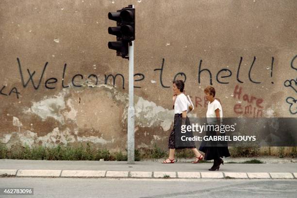 Two women walk across the area of Sarajevo known as "Sniper Alley" on August 24 1993, near a wall with graffiti that reads "Welcome to Hell." The...