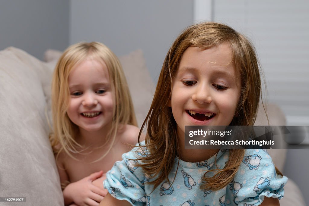 Two young sisters laughing together on a couch