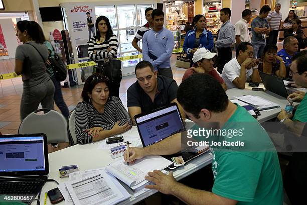 As people stand in line to speak with an insurance agent Marlene Lima-Rodriguez and Javier Gonzalez sit with Denis Garcia an insurance agent from...