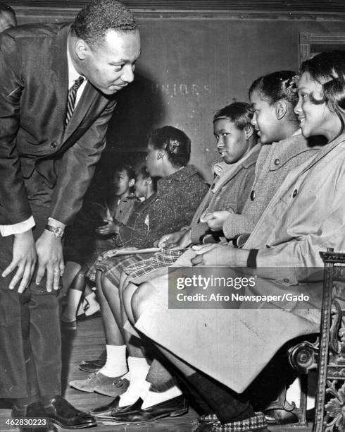 American Civil Rights and religious leader Dr Martin Luther King Jr bends down as he speaks with a group of schoolgirls in a classroom, January 1960.