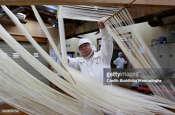 Japanese somen maker, Yoshinobu Izuhara, uses chopsticks to stretch drying Ibonoito somen noodles on February 6, 2015 in Tatsuno, Japan. Somen is a...