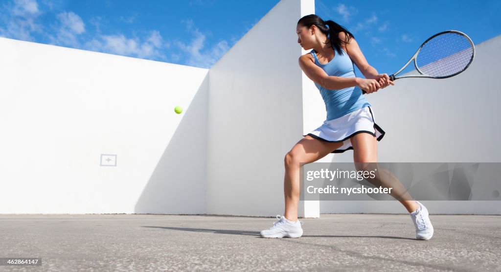 Young female hitting tennis ball against a wall