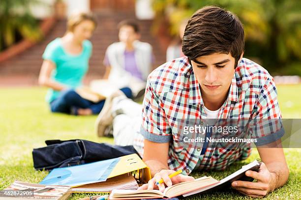 hombre leyendo libro con grupo de estudiantes en el campus de fondo - one teenage boy only fotografías e imágenes de stock