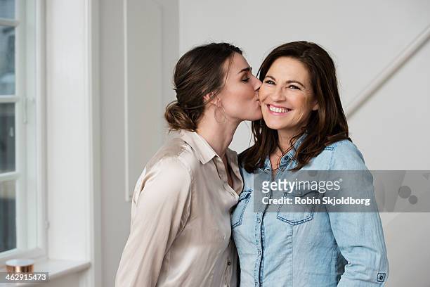 daughter kissing mature mother on cheek - moeder dochter stockfoto's en -beelden