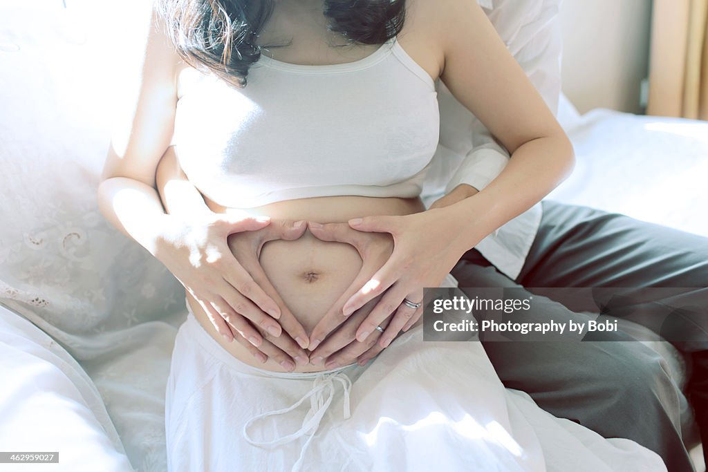 Couple hands make a heart on pregnant belly