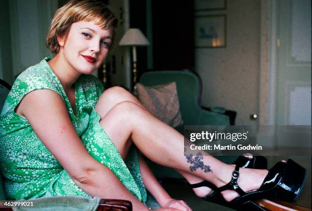 American actress in a green dress and black patent platforms, with a tattoo of a cross on her calf, photographed in her hotel room in London, 25th...