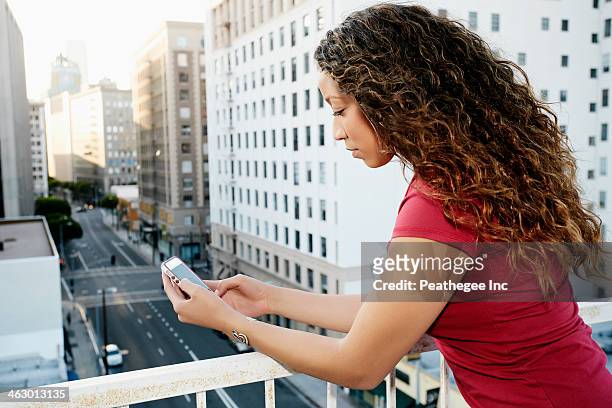 mixed race woman using cell phone on urban rooftop - social media profile stock pictures, royalty-free photos & images