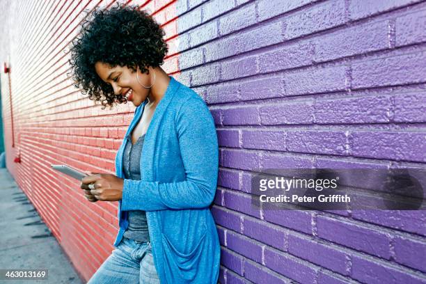 mixed race woman with cell phone standing by colorful wall - black brick wall fotografías e imágenes de stock