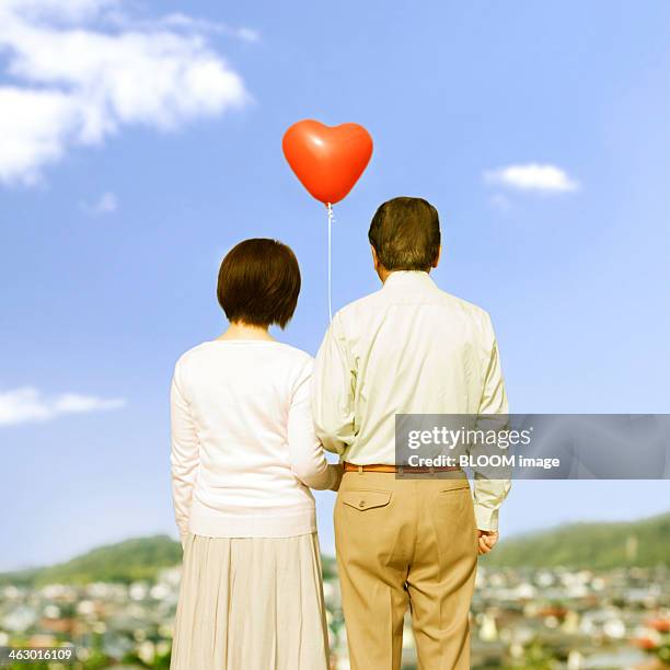 portrait of a senior couple holding a red balloon - two houses side by side stock pictures, royalty-free photos & images