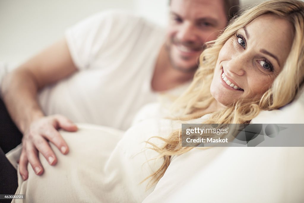 Portrait of happy pregnant woman with man lying in bed