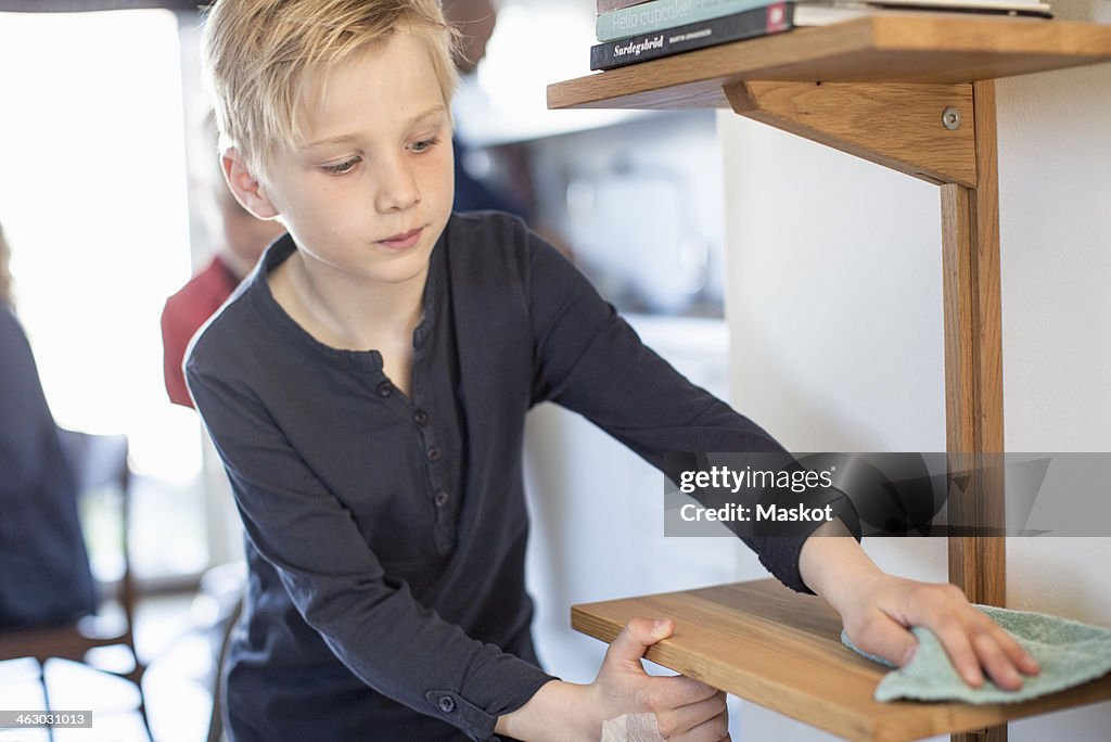 Boy cleaning shelf in house