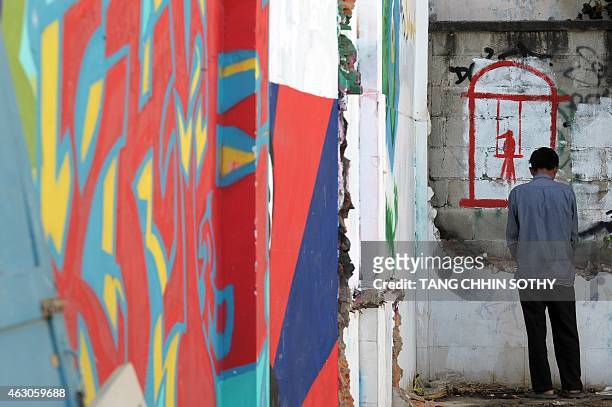 Cambodian man urinates next to a wall with graffiti artworks upon it at the Boeung Kok community in Phnom Penh on February 9, 2015. AFP PHOTO / TANG...