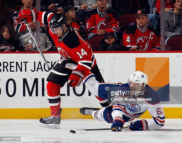 Iiro Pakarinen of the Edmonton Oilers is tripped up by Adam Henrique of the New Jersey Devils during the second period at the Prudential Center on...