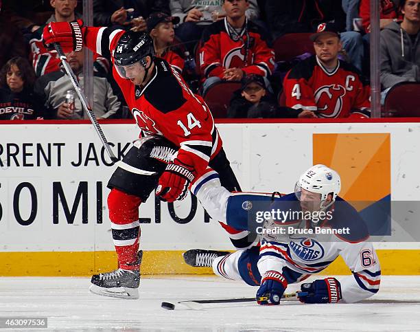 Iiro Pakarinen of the Edmonton Oilers is tripped up by Adam Henrique of the New Jersey Devils during the second period at the Prudential Center on...