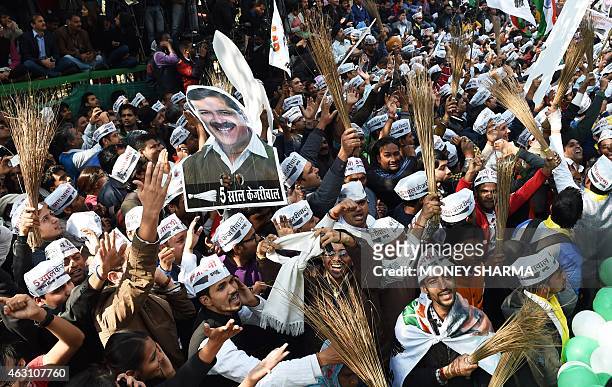 Indian supporters of the Aam Aadmi Party wave brooms, the party symbol, and posters bearing the image of party leader Arvind Kejriwal as they...