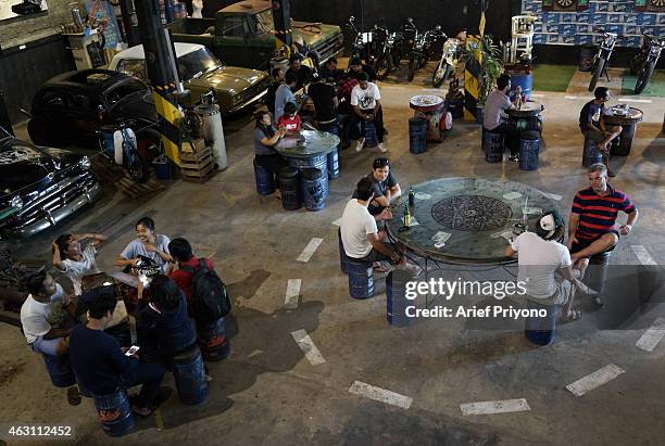 Visitors enjoy hanging out in the garage full of old motorcycles and cars, in ManShed Cafe, Sanur. The ManShed cafe in Sanur, Bali is themed on an...