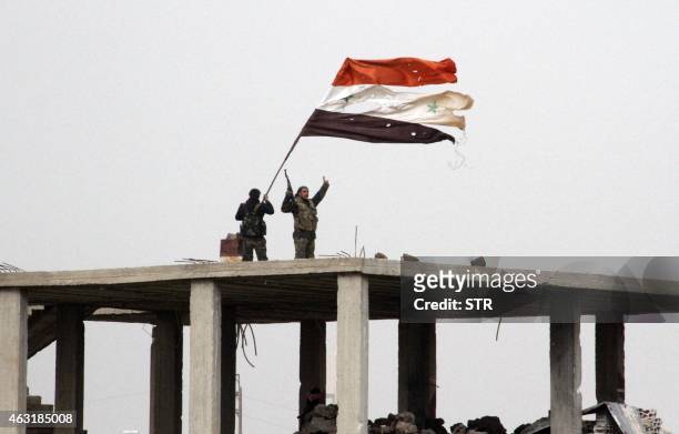 Syrian government forces wave the Syrian flag while standing on top of a building in Deir al-Adas in the Daraa province on February 11, 2015 after...