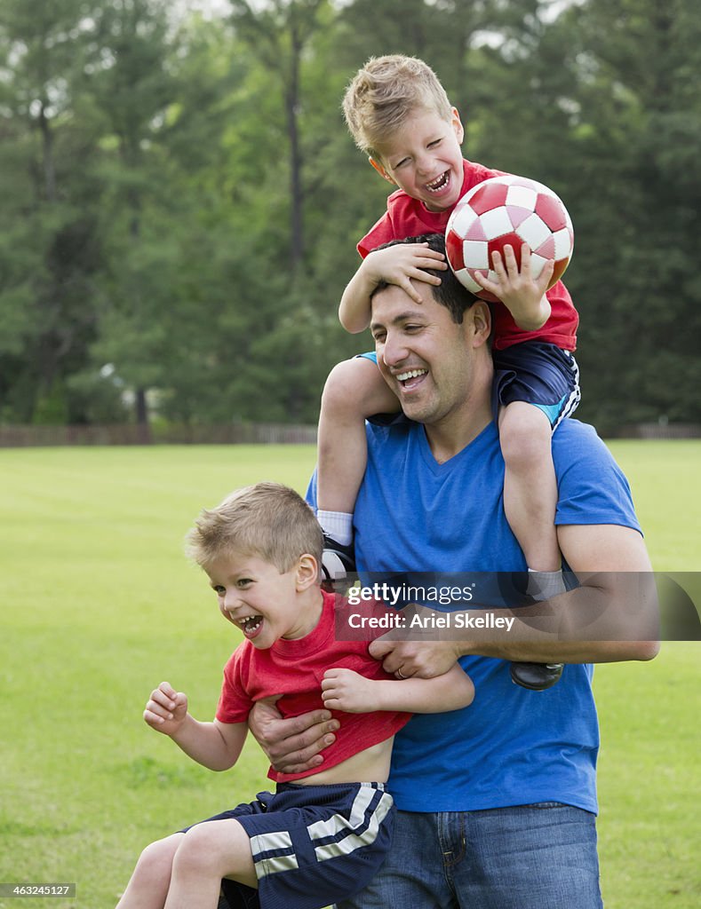 Father and twin  sons playing on soccer field