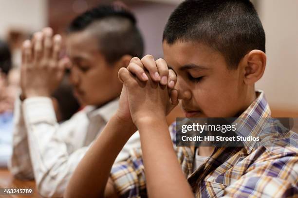 hispanic boys praying in church - niños orando fotografías e imágenes de stock