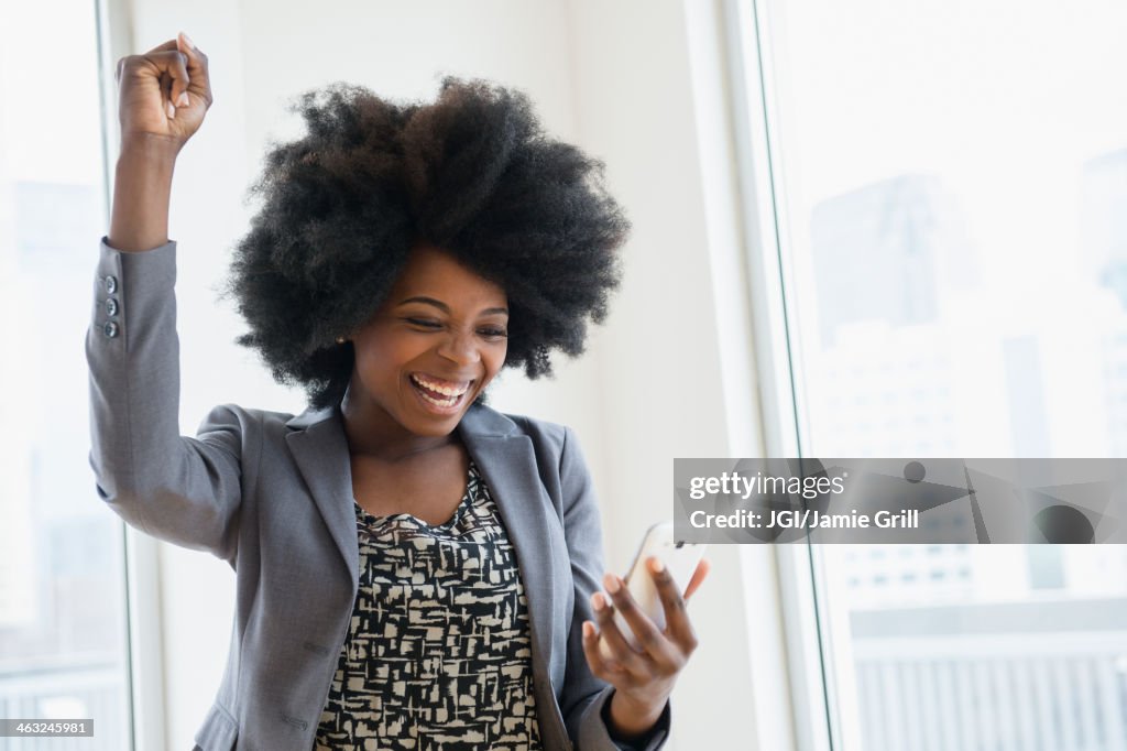 Mixed race businesswoman holding cell phone and cheering