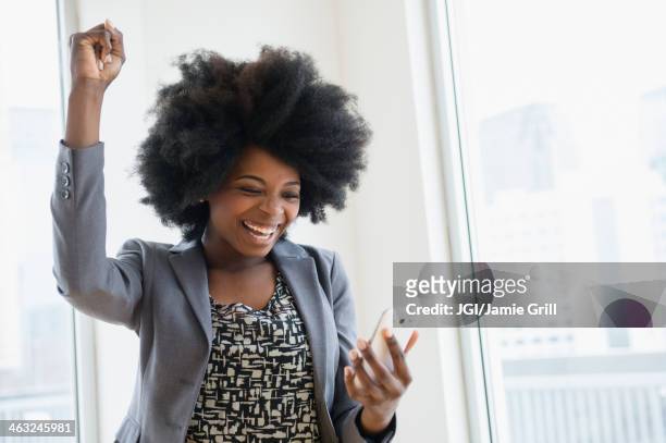 mixed race businesswoman holding cell phone and cheering - business woman cheering stockfoto's en -beelden