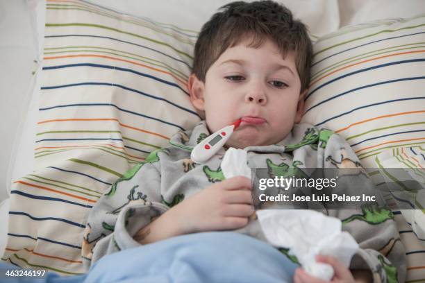 boy laying in bed with thermometer in mouth - fieber stock-fotos und bilder