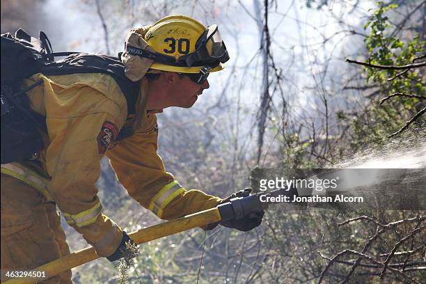 Firefighter Jeff Newby sprays water on a flare-up at the Colby Fire burning for a second day in the hillside above Highway 39 on January 17, 2014 in...