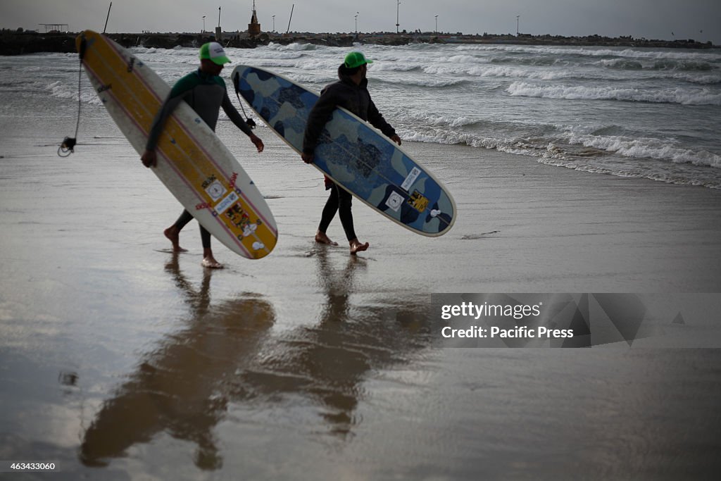 Palestinian surfers carry their surfboards as they wade in...