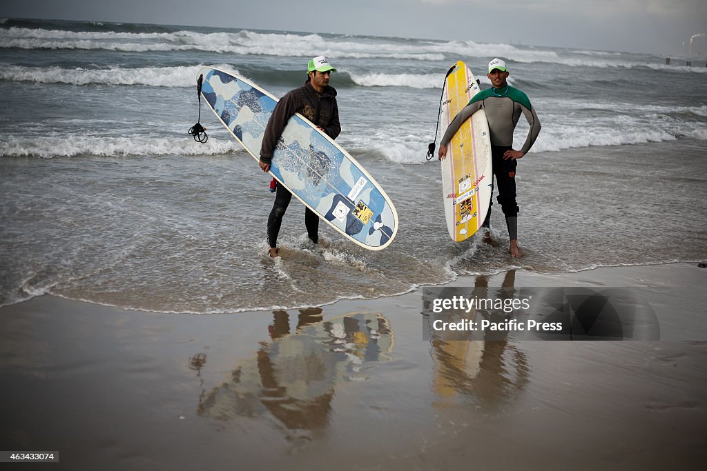 Palestinian surfers carry their surfboards as they wade in...