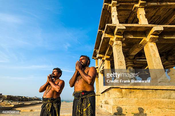Two Devotees are praying at the Temples on Hemakuta Hill, a part of the ruins of the former Vijayanagara Empire, which was established in 1336 by...