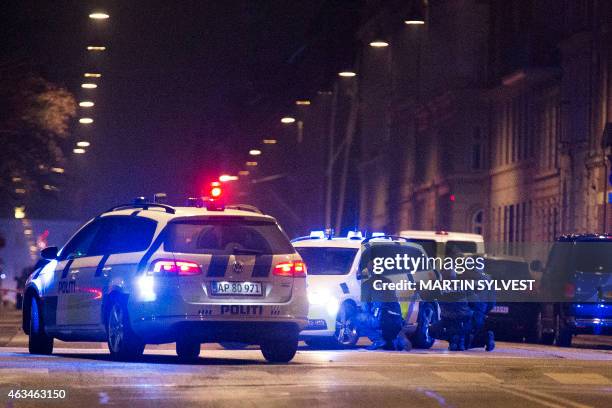 Police officers take cover behind their patrol cars on the streets of central Copenhagen on February 15, 2015 after one person was shot in the head...