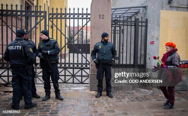 Heavily armed police officers watch a woman arriving to lay flowers outside the main Synagogue in Copenhagen on February 15, 2015 following two fatal...