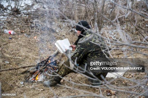 Ukrainian serviceman reads a book as he warms himself by a camp fire in Svitlodarsk, approaching Debaltseve on February 15, 2015. A ceasefire in...