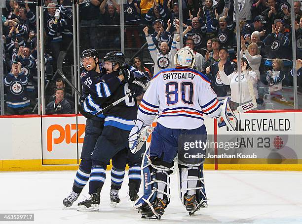 Goaltender Ilya Bryzgalov of the Edmonton Oilers skates off the iec as Blake Wheeler and Jacob Trouba of the Winnipeg Jets celebrate an overtime goal...