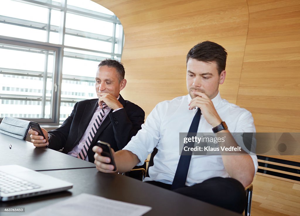 2 businessmen in same position, tjecking phones
