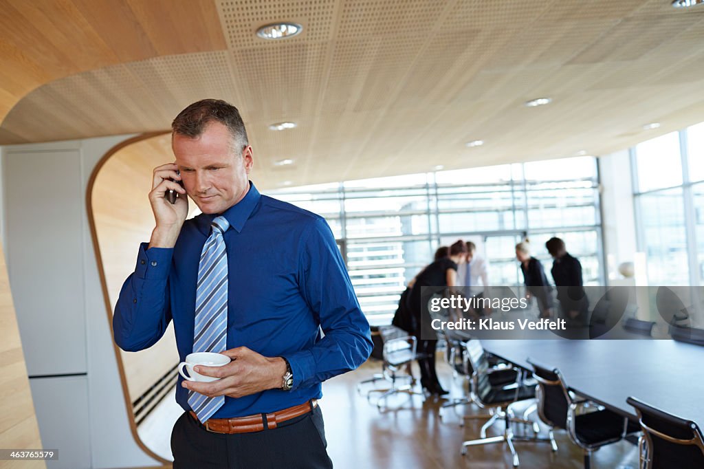 Businessman holding up phone, coworkers in back
