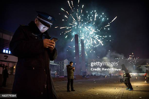 February 19: A Chinese security guard checks his smartphone as fireworks explode during celebrations of the Lunar New early on February 19, 2015 in...