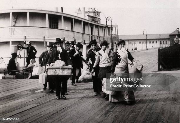 Immigrants to the USA landing at Ellis Island, New York, c1900. They head for the processing centre, each carrying a paper with an entry number which...