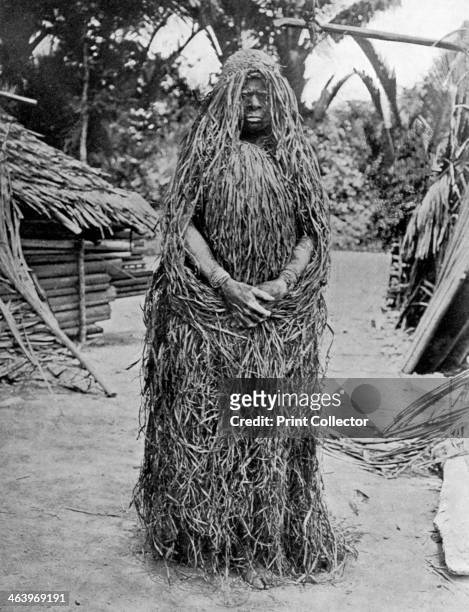 Woman wearing full mourning costume, Melanesia, 1920. After the death of a man his wife is secluded in an enclosure of mats, she smears her body in...